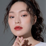 Model wearing Muzigae Mansion Objet Liquid Lip Tint in Dominant 008, demonstrating the shade in natural lighting