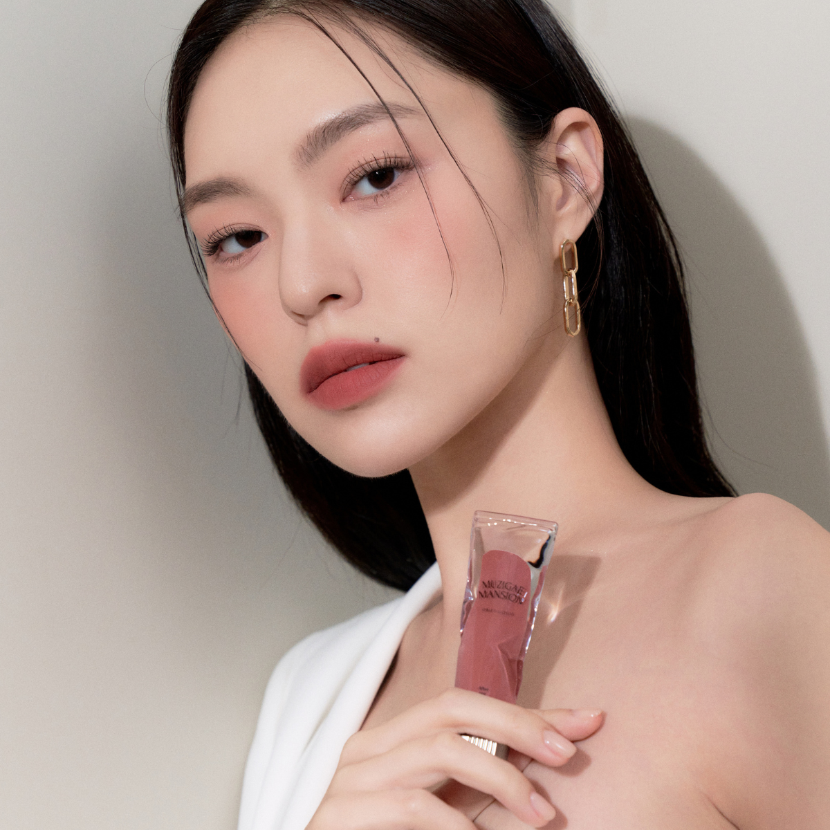 Model wearing Muziage Mansion Objet Liquid Lip Tint in After 016, demonstrating the shade in natural lighting and holding product