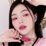 Model wearing Muziage Mansion Objet Liquid Lip Tint in Knockout 018, demonstrating the shade in natural lighting